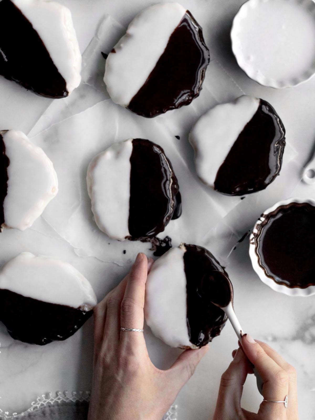 Hands add chocolate glaze to half of a nyc black and white cookie.
