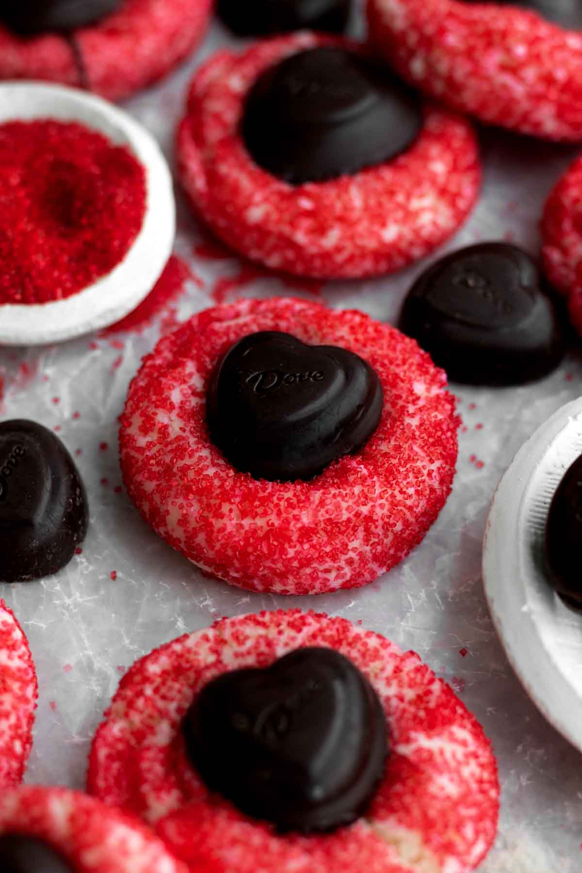 Sugar Cookie Blossoms sit on parchment paper with red sugar crystals and heart-shaped chocolates.