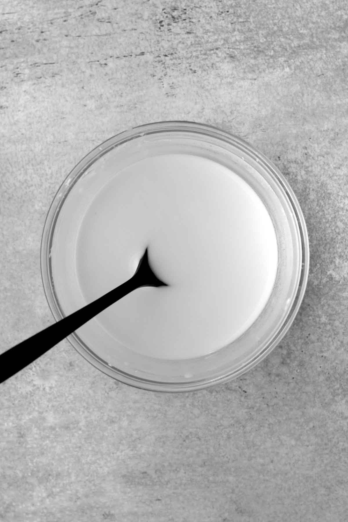 A glass bowl with a spoon in a viscous mixture of cornstarch and water.