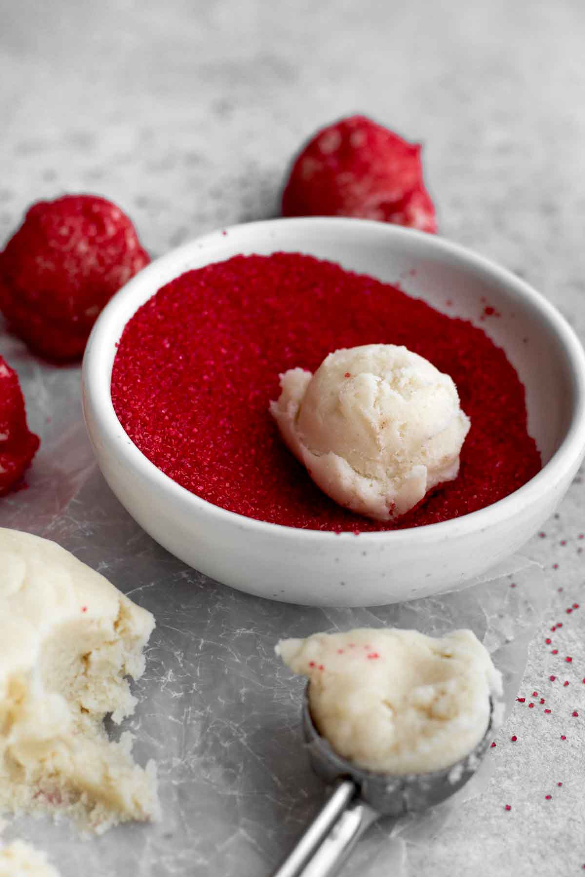 A small ball of cookie dough sitting in a bowl of red sugar about to be coated.