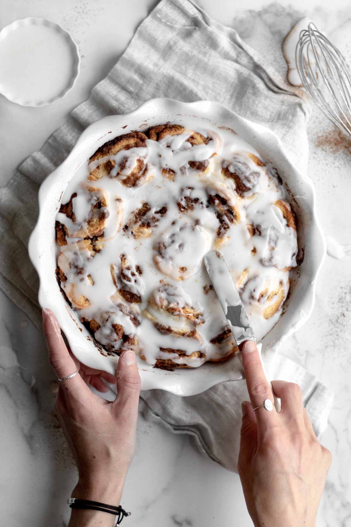 Spreading generous portions of sugary glaze onto the gluten free Cinnamon Rolls.