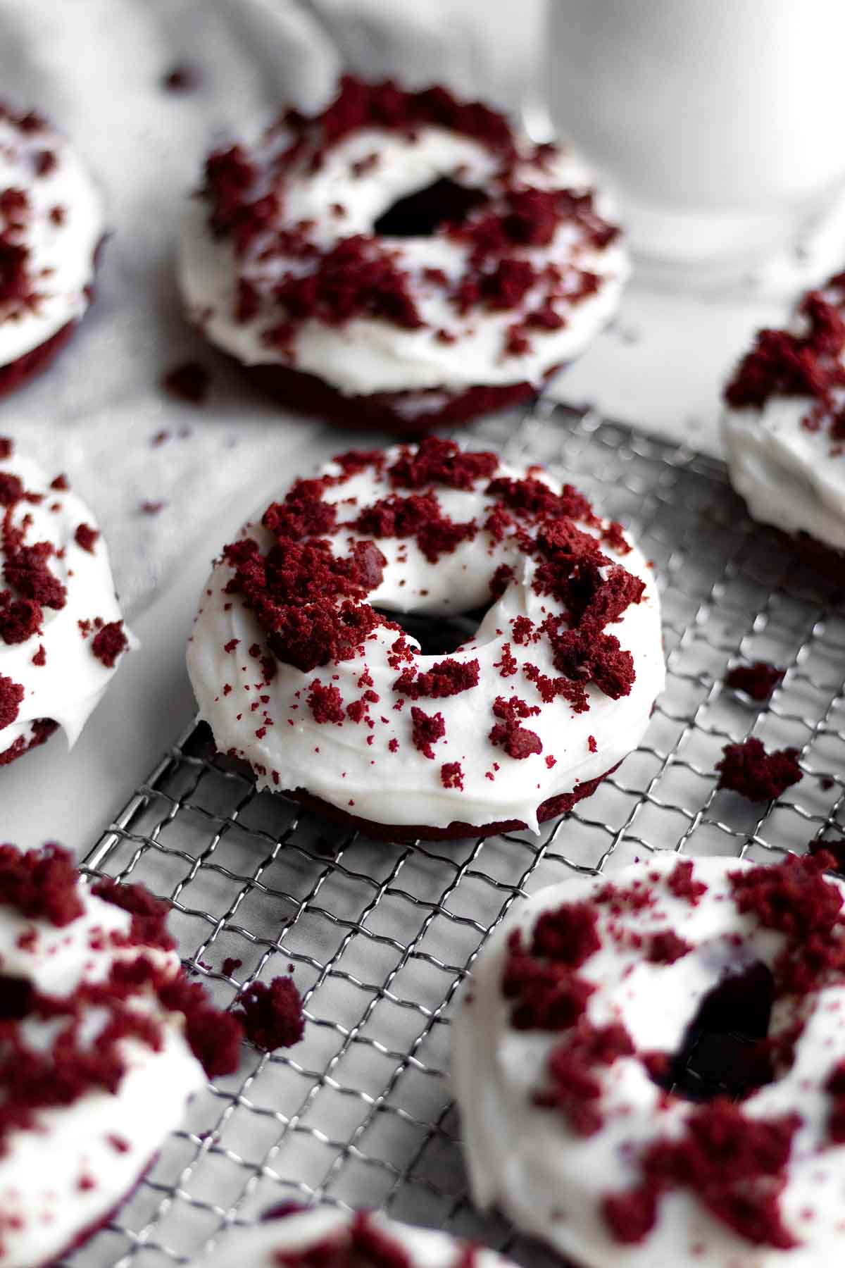 A Red Velvet Donut with white frosting and red velvet crumbs.