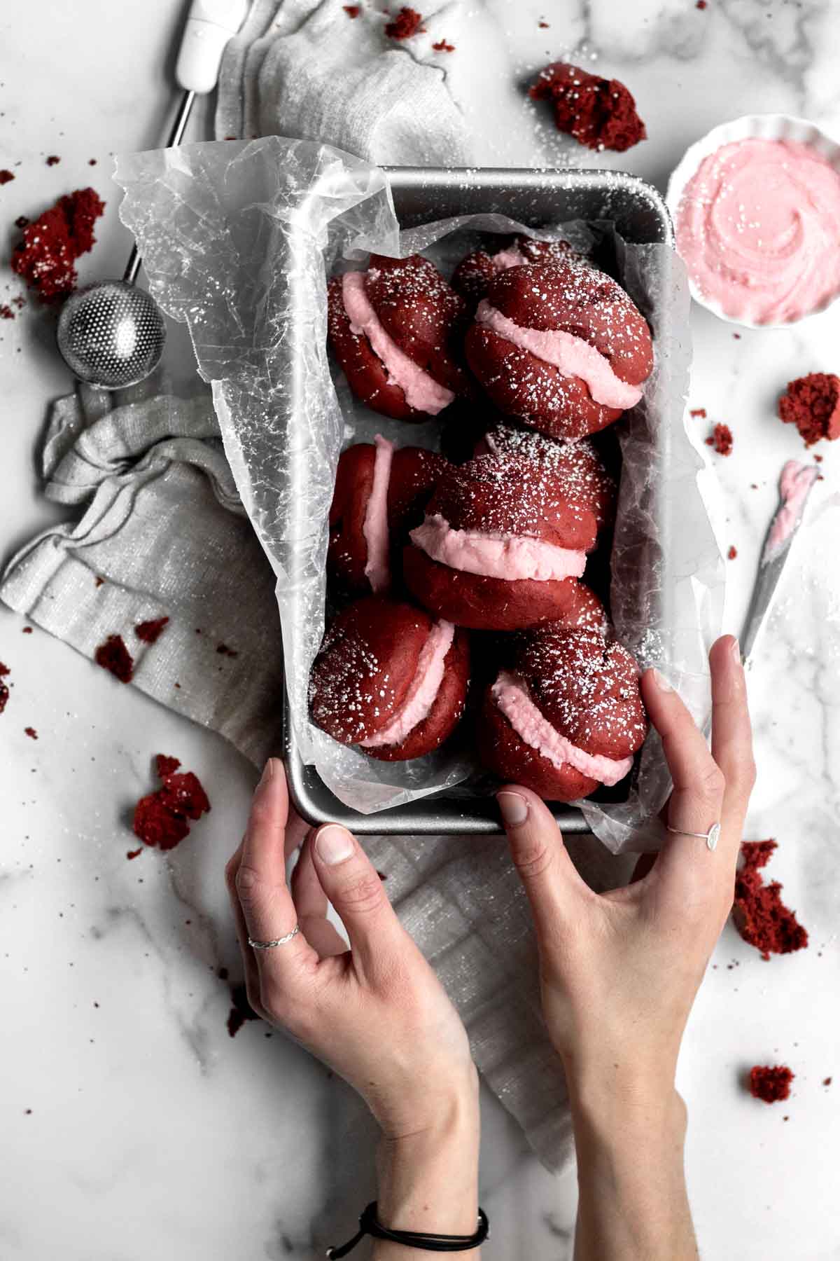 A hand reaches for a gluten free Red Velvet Whoopie Pie.