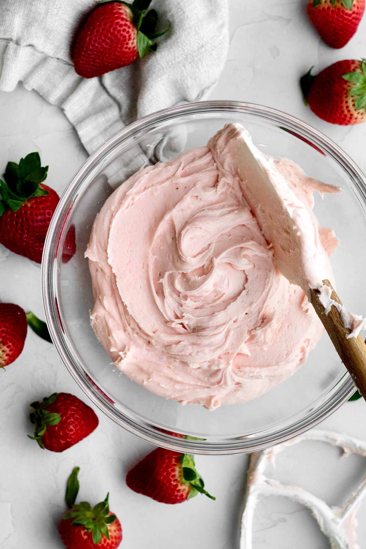 A bowl of gluten free Strawberry Buttercream stirred by a spatula.