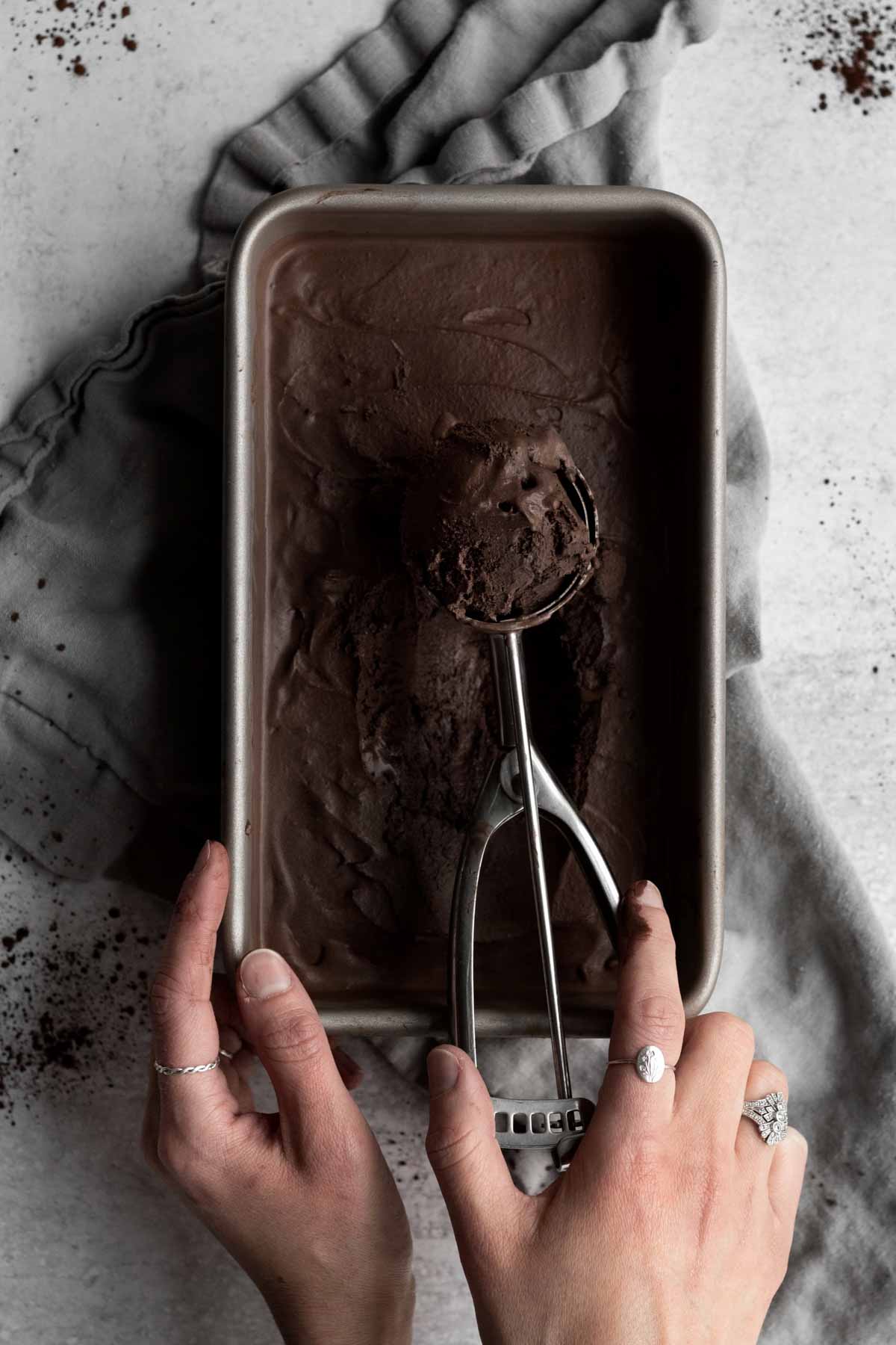 Hands take a scoop of Chocolate Ice Cream from a pan.