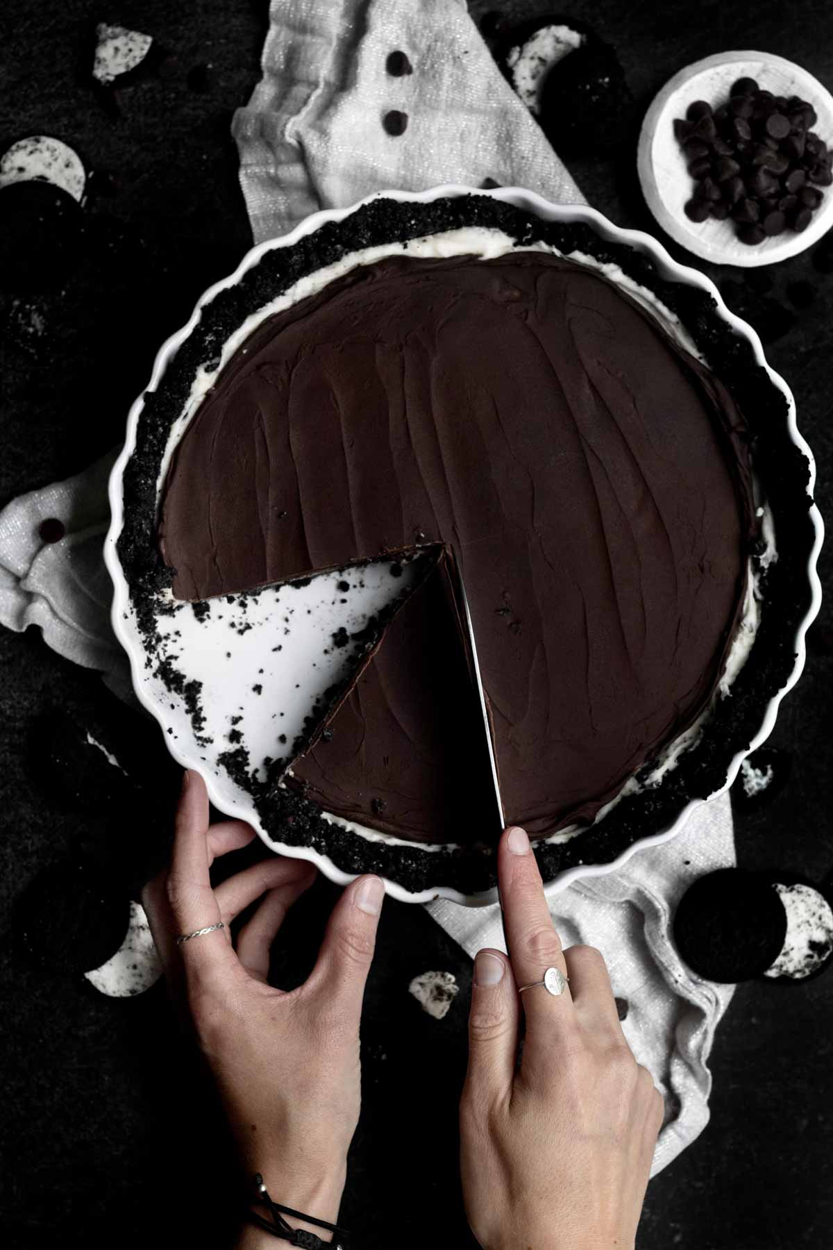 Hands carve a slice out of the dark Cookies and Cream Pie.
